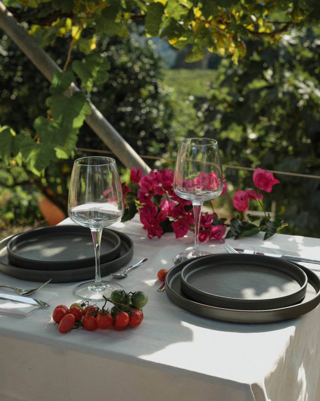 Tischdekoration im Garten mit schwarzem Keramikgeschirr, Blumen und frischen Tomaten