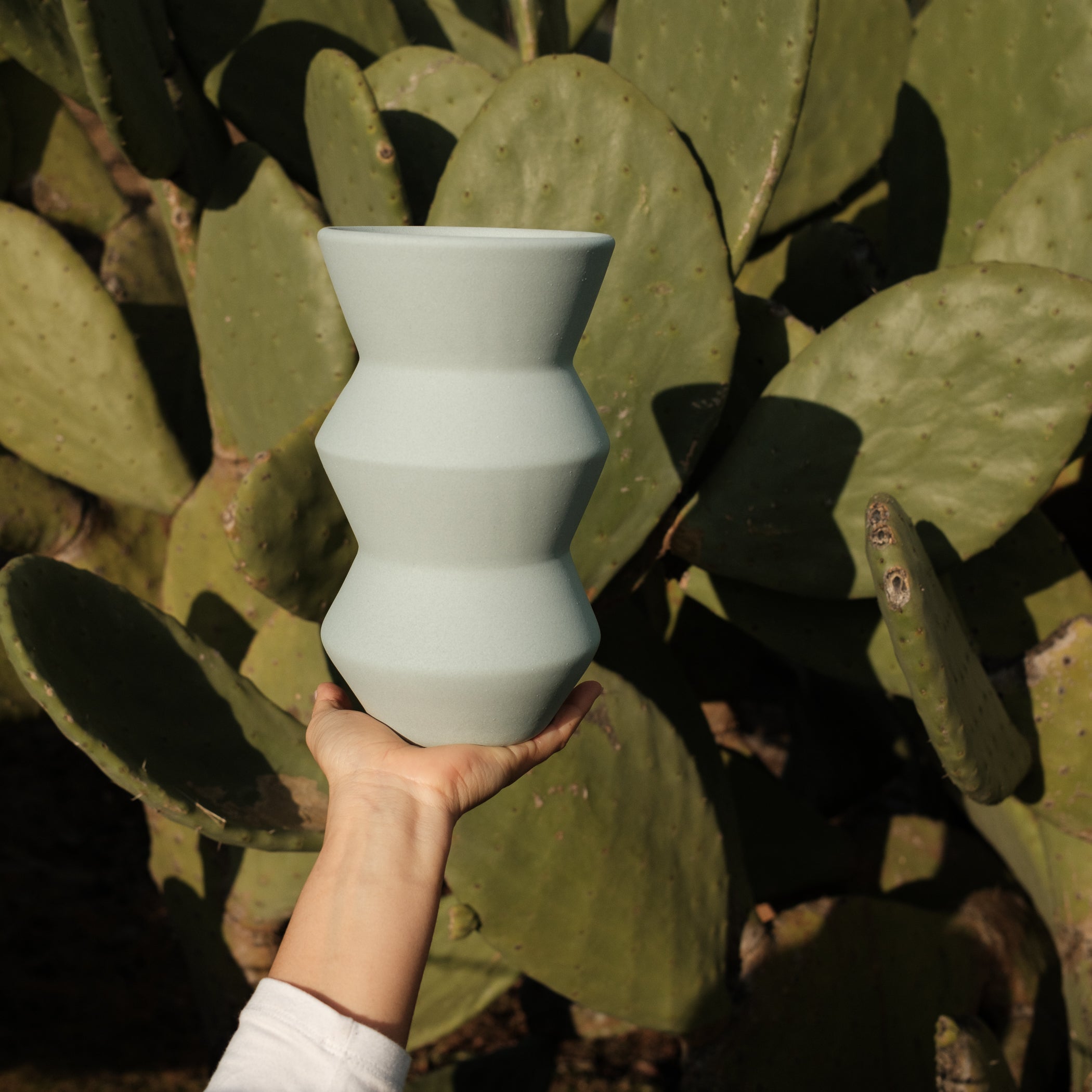 Eine Hand hält eine zickzackförmige Keramikvase im Hintergrund ist ein Kaktus zu sehen